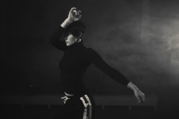 Fototapeta na wymiar modern beautiful dancer in black clothes posing against the Studio in the smoke
