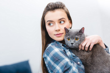 girl holding british shorthair cat and looking away at home