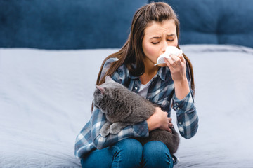 girl with allergy holding facial tissue and british shorthair cat at home