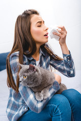 young woman with allergy holding facial tissue and british shorthair cat