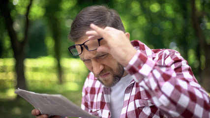 Male trying to read newspaper in park, poor sight, farsightedness, myopia