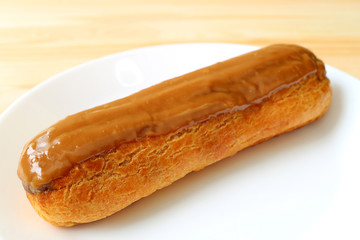 One Delicious Caramel Eclair Served on White Plate, Selective Focus and Blurred Background 