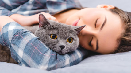 close-up view of girl sleeping on bed with british shorthair cat