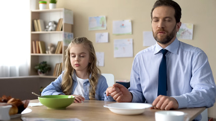 Pretty girl and her father praying before eating breakfast, spiritual education