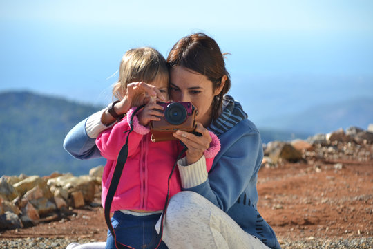 Mom teaches her daughter to taking pictures. Mom and her little kid holding camera together and taking picture in the mountains.