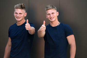Everything is all right. Athletic men show thumbs ups. Pair of twins with muscular look. Muscular men in good physique. Fashion twins with fit body. Handsome twins in casual fashion style