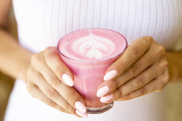 Woman is holding vegan organic pink matcha with white dress background.