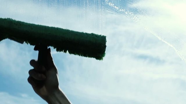 Man washes a dirty window on the balcony, an industrial climber lathers the window outside in slow motion, close-up