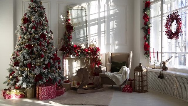 White room interior in red tones with New Year tree decorated, present boxes and artificial fireplace