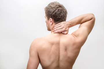 Shirtless young man stand and hold hand on neck. He feels pain there. Guy shows his back. Isolated...
