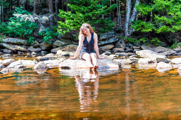Young happy smiling woman enjoying nature on peaceful, calm Red Creek river in Dolly Sods, West Virginia during sunny day with reflection dipping feet in water