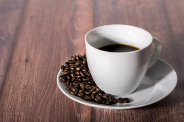 Roasted coffee beans and cup of coffee on wooden table