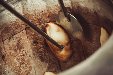 Baker making turkish pita bread in tandoor (clay oven). Baking process. Many fresh hot bread in the basket