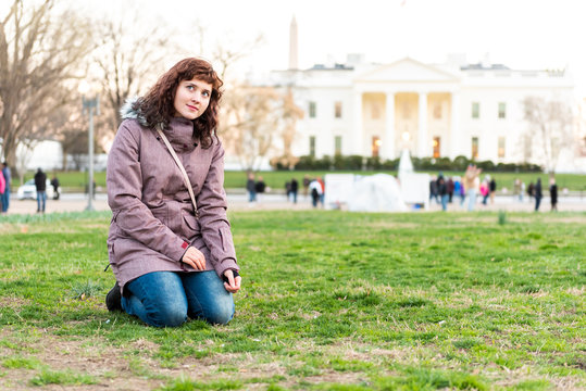 Young woman sitting in green grass lawn, in park in front of White House at sunset in Washington DC