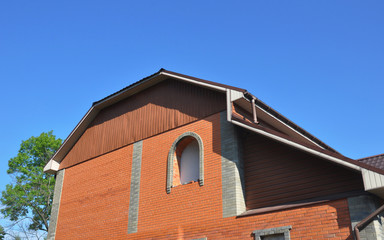 Fototapeta na wymiar House mansard roof with brick wall, unfinished window installation, rain gutters.