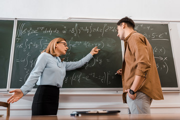 Female professor pointing at equations to student in classroom