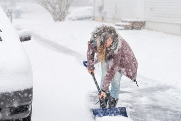 Young woman, female in winter coat cleaning, shoveling driveway, street from snow in heavy snowing...