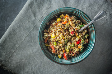 Quinoa salad bowl with various vegetables: green beans, carrot, corn, bell pepper, peas on a table with a spoon in the bowl. Top view, copy space.