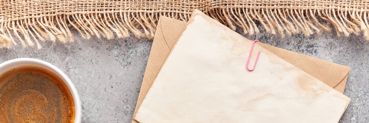 Top view of blank brown old envelope with hot coffee cup and jute bag on the stone table top. Mock...
