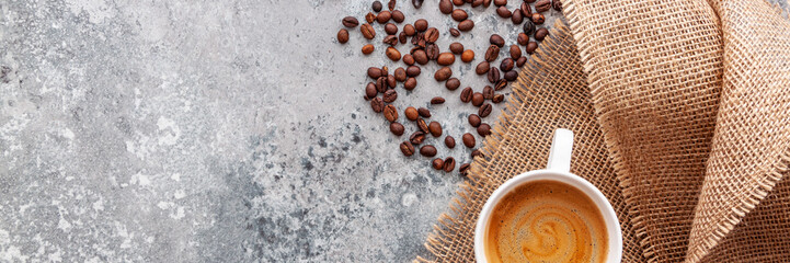 Coffee beans and cup of coffee on the natural stone texture. Copy space background. Jute bag...