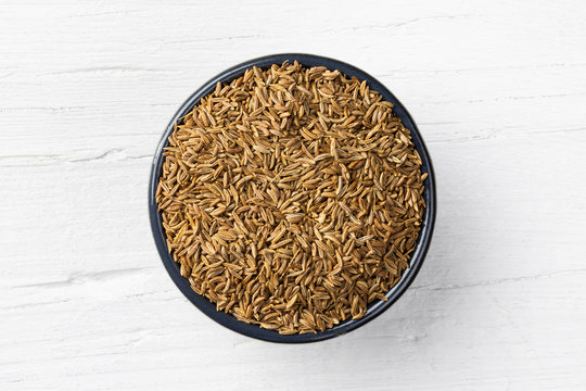Caraway seeds on white wooden background,