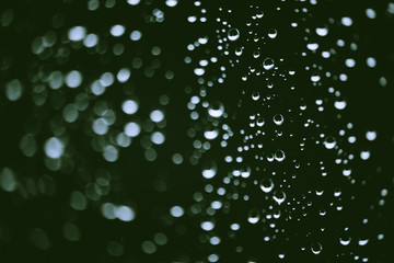 Dirty window glass with drops of rain. Atmospheric green background with raindrops in bokeh. Droplets and stains close up. Detailed transparent texture in macro with copy space. Rainy weather.