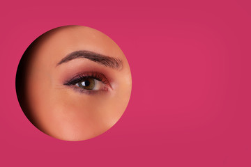 Girl with bright eyes make up looks through hole of pink paper. Business card of artist, beauty concept. Ready to new year party. Cosmetics sale. Beauty salon advertising banner with copy space - obrazy, fototapety, plakaty