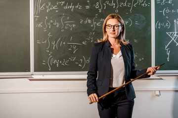 attractive female teacher with wooden pointer explaining mathematical equations in classroom