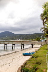 Obraz premium Wooden pier of Morrinhos beach, with wooden fishing boat and Zimbros beach in the background, Bombinhas, Santa Catarina