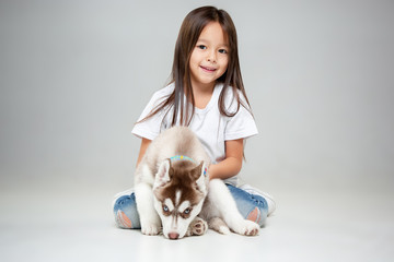 Portrait of a joyful little girl having fun with siberian husky puppy on the floor at studio. The animal, friendship, love, pet, childhood, happiness, dog, lifestyle concept © master1305