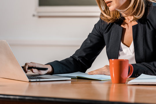 cropped view of teacher using laptop and sitting at desk