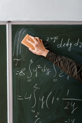 cropped view of male student wiping mathematical equations with sponge in classroom