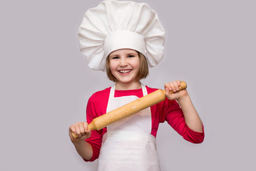 Children cook. Happy little girl in chef uniform holds rolling pin isolated on white background.