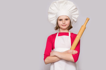 Children cook. Happy little girl in chef uniform holds rolling pin isolated on white background.