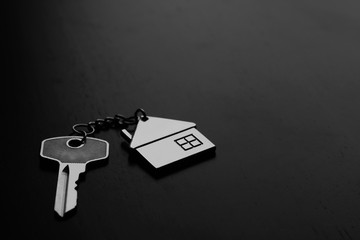 Home key with house keyring on black wood table in dark tone, real estate concept