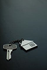 Home key with house keyring on black wood table in dark tone, real estate concept