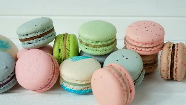 Multicolored macaroons or macarons lie on a white wooden background, a row of almond cookies. Video in slow motion