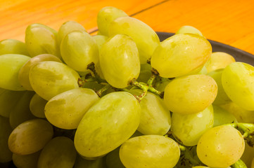 large brush of green grapes in a dark ceramic plate on a wooden background