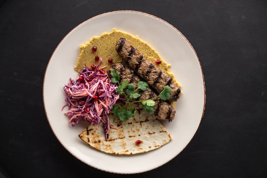 Indian style shish kofta kebab with pickled onion and pita bread on black background