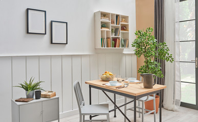 Living room corner dining room style, white and brown wall, white shelf and frames on the wall. Wooden dining table decorative style with chair.