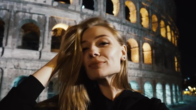 Tourist on the background of the night coliseum. She takes a selfie. Posing.