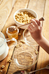 Kids hand holding bowl with healthy breakfast with flakes honey milk and honey dipper on old wooden table