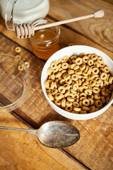 Healthy morning breakfast bowl full of honey flakes with honey dipper and milk on an old wooden table