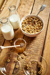 Healthy morning breakfast bowl full of honey flakes with honey dipper and milk on an old wooden table