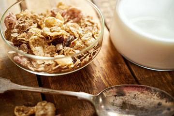 Healthy morning breakfast bowl full of organic granola with a spoon and a jug of milk on an old wooden table