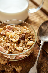 Healthy morning breakfast bowl full of organic granola with a spoon and a jug of milk on an old wooden table