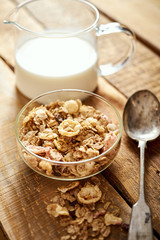 Healthy morning breakfast bowl full of organic granola with a spoon and a jug of milk on an old wooden table