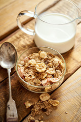 Healthy morning breakfast bowl full of organic granola with a spoon and a jug of milk on an old wooden table