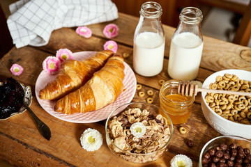 Healthy morning breakfast with different types of breakfast cereal with honey marmalade croissants and milk on old wooden table
