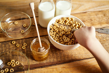 Kids hand holding bowl with healthy breakfast with flakes honey milk and honey dipper on old wooden table